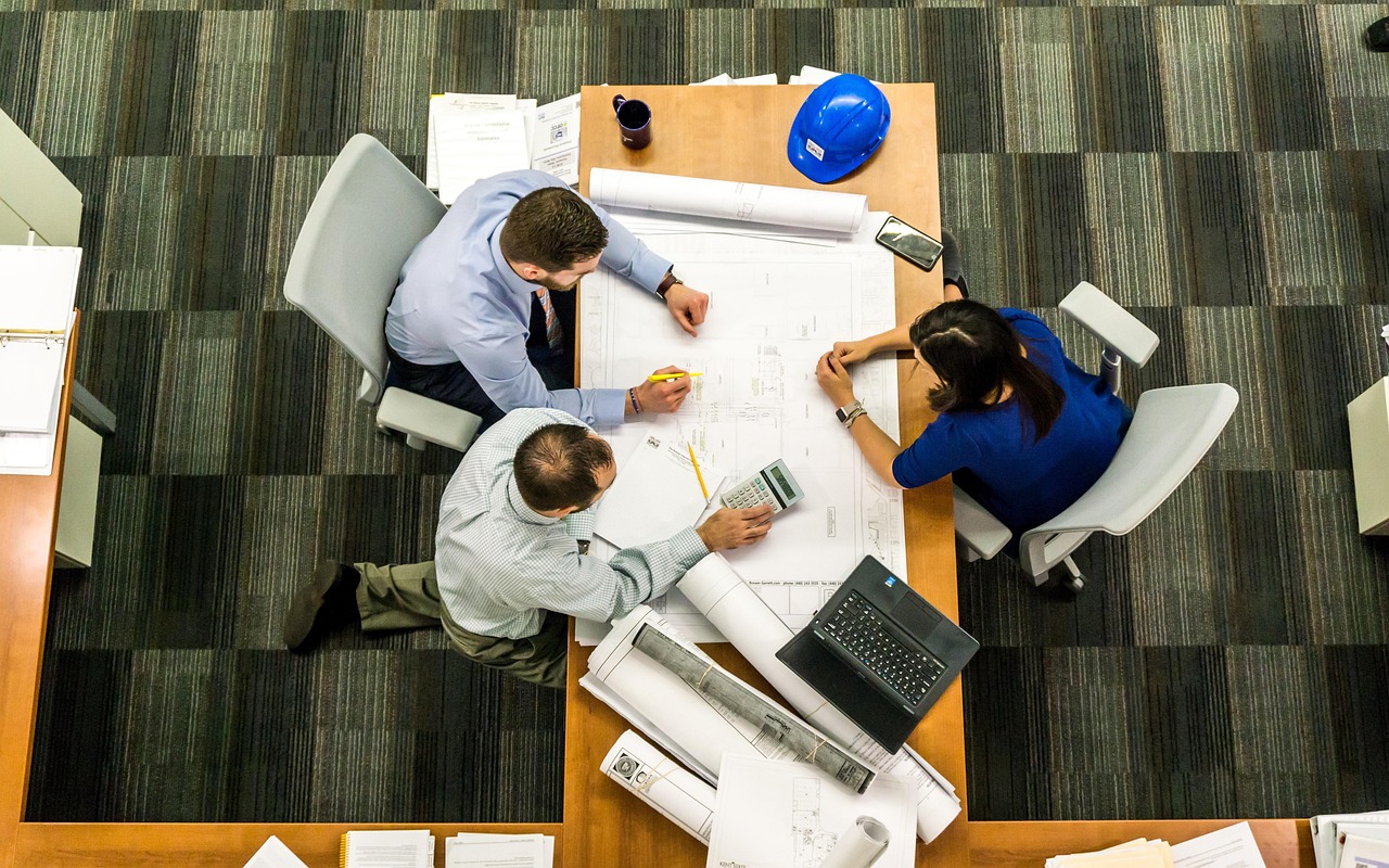 Reunião de planejamento financeiro com 3 pessoas para decidir entre consórcio ou financiamento, com muitos papeis sobre a mesa.