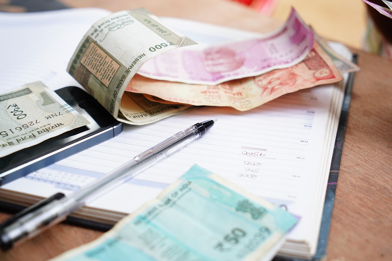 Dinheiro, caderno e caneta numa mesa representando o planejamento da reserva financeira para conter gastos.
