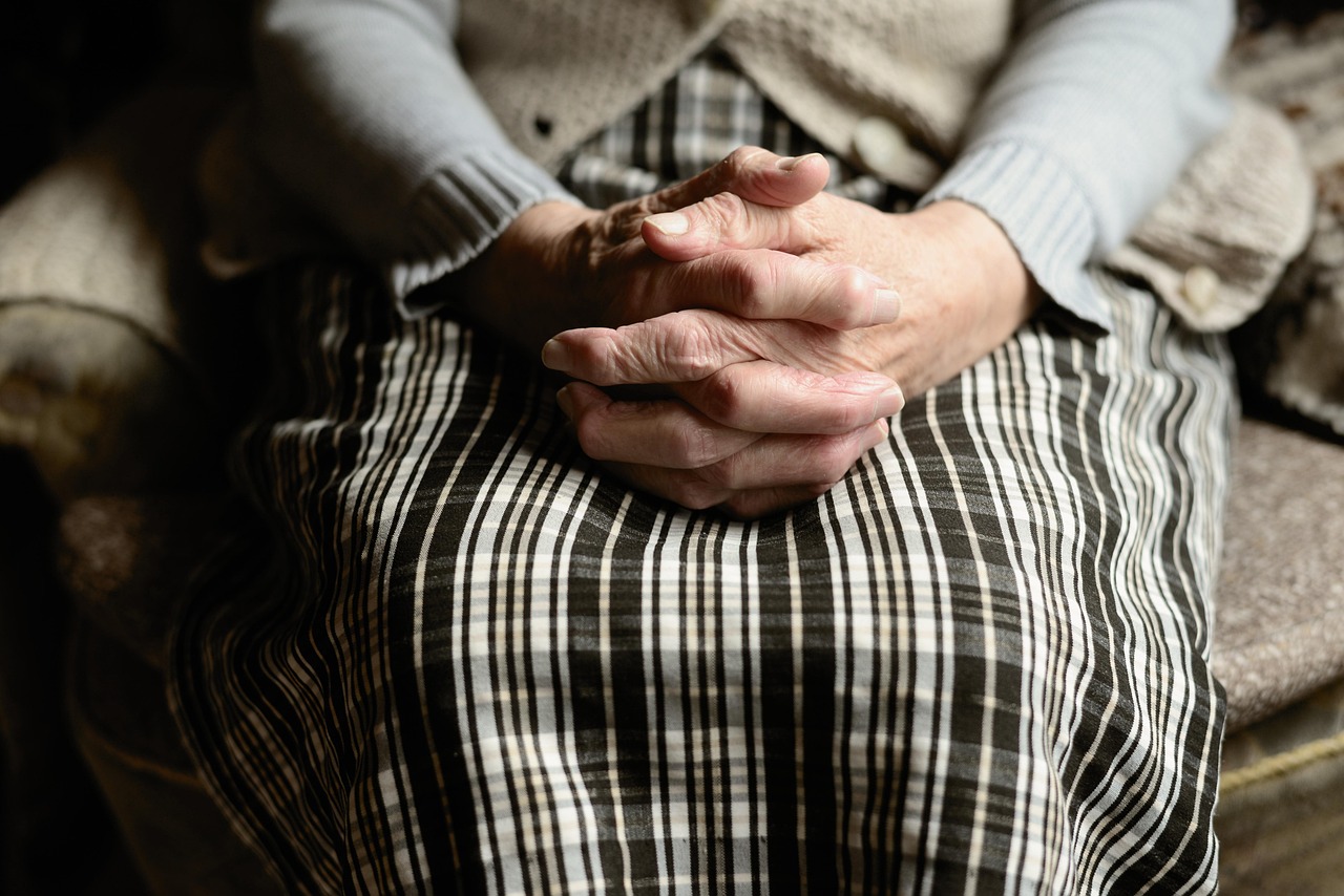 Mulher idosa sentada com as mãos entrelaçadas representando planejamento de longo prazo e previdência privada.