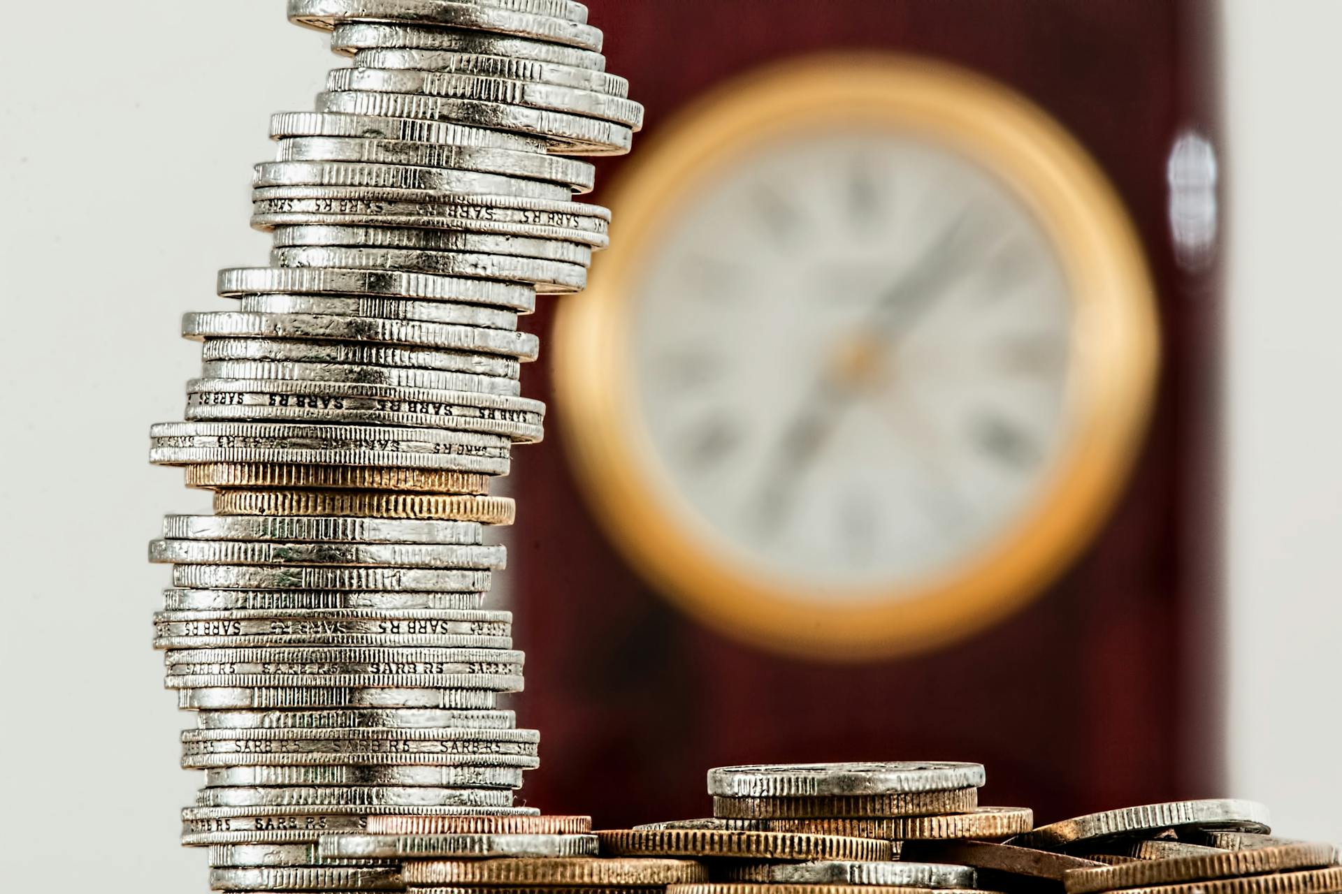 Moedas empilhadas com um relógio ao fundo